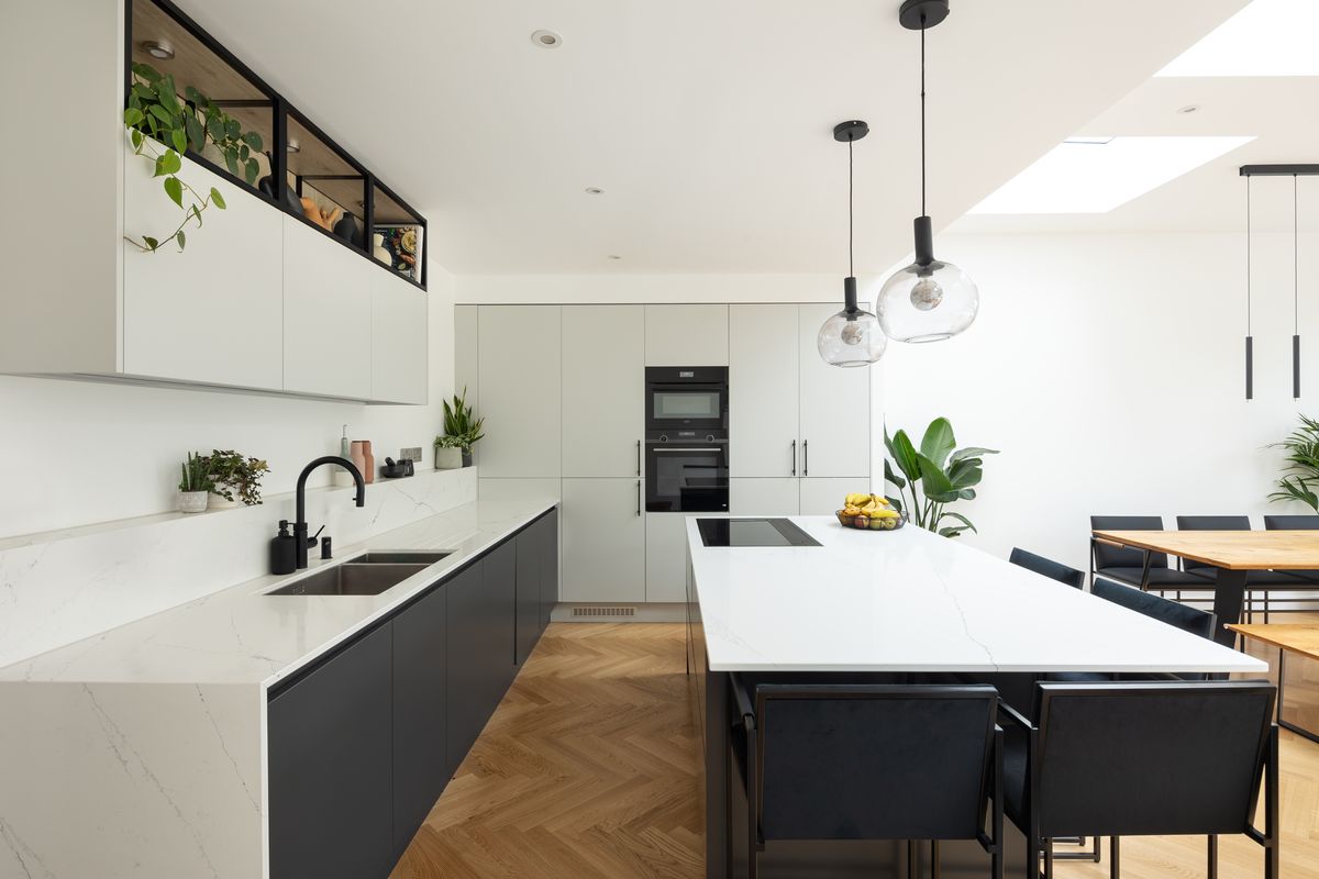 White kitchen with island, glass pendant lights and herringbone floor – Headington Road by MyLondonExtensions. Photograph by Daniel Avery.
