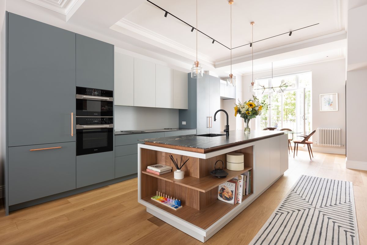 Open-plan kitchen with grey-blue cabinetry, walnut-shelved island and track lighting – Lower Addison Gardens by Hone Studio. Photograph by Daniel Avery.